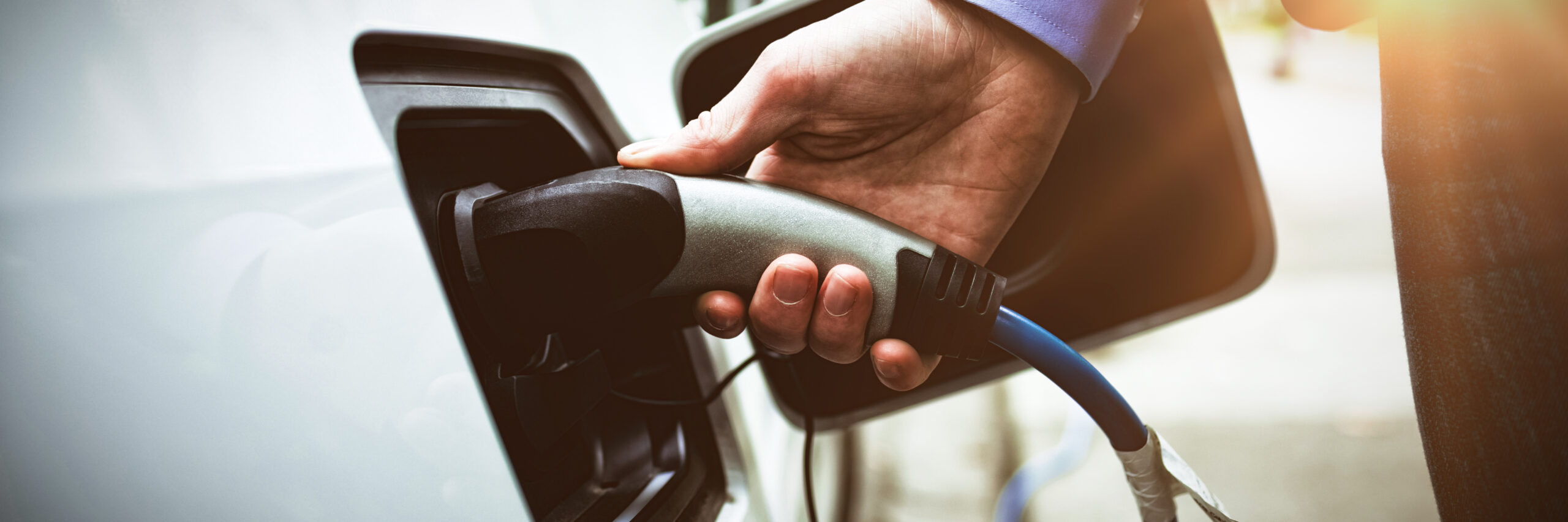 Close-up of businessman charging electric car at charging station
